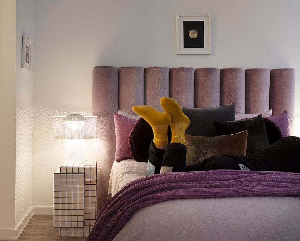 hình ảnh một góc phòng ngủ trong căn hộ nhỏ với đèn đầu giường, bàn hình khối rubik độc đáo, chăn gối màu tím trắng