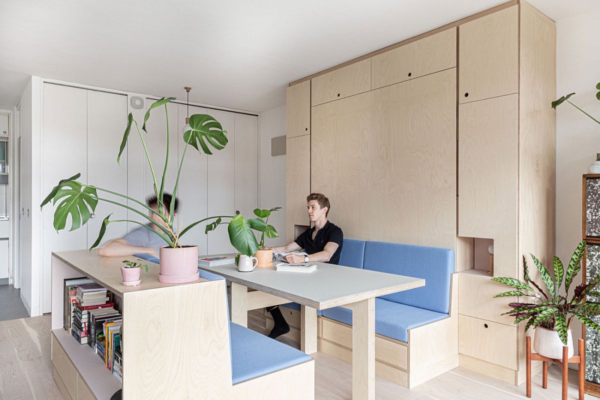 hình ảnh phòng ăn trong căn hộ studio nhỏ ở London với bàn ghế gỗ lót nệm màu xanh, hai chàng trai trẻ