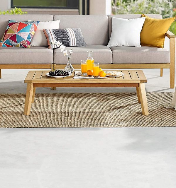 hình ảnh bàn cà phê ngoài trời bằng gỗ bạch đàn đặt trên thảm cói, cạnh đó là ghế sofa xám khung gỗ, gối tựa màu sắc