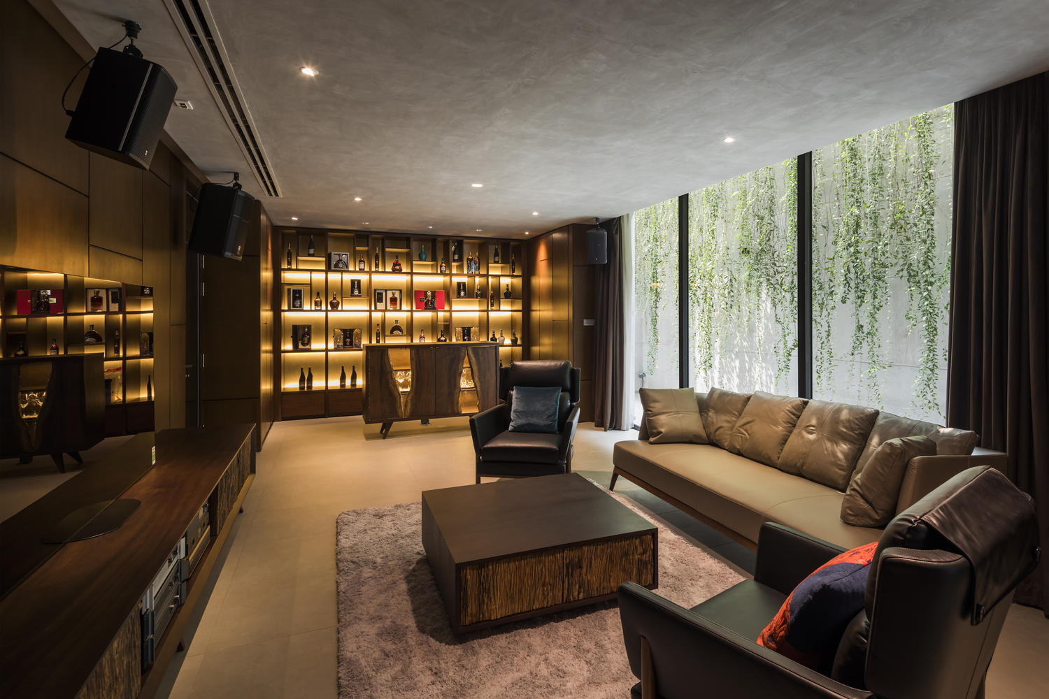 hình ảnh phòng sinh hoạt chung trên tầng lầu sang trọng với sofa bọc da màu xám, bàn trà gỗ vuông đặt trên thảm lông, cạnh đó là hệ tủ rượu ấn tượng với đèn LED vàng trang trí