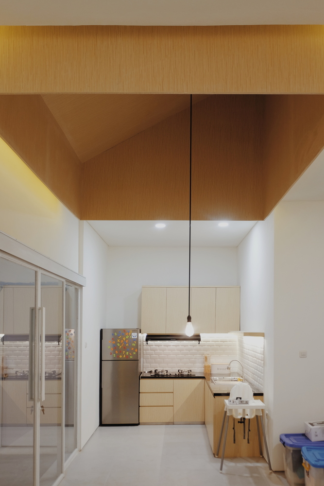 hình ảnh phòng bếp ngôi nhà sau cải tạo trở nên gọn gàng hơn với hệ tủ gỗ gắn tường, tủ lạnh nhỏ đặt ở góc, đèn chiếu sáng đầy đủ