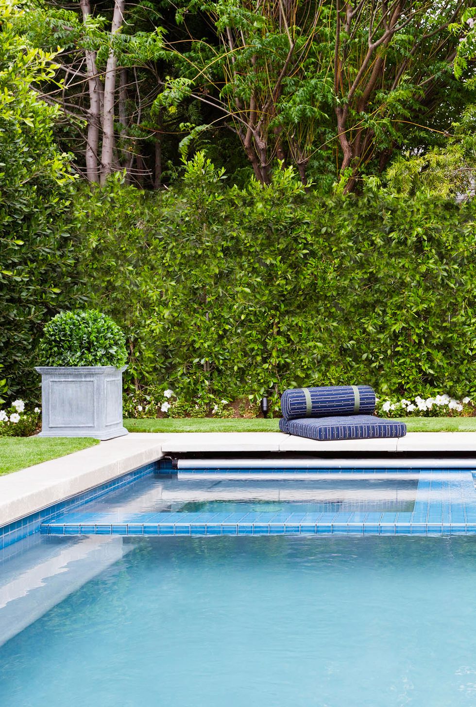 hình ảnh cận cảnh một góc bể bơi trong xanh ở sân sau nhà, phía trên đặt đệm nằm tắm nắng, xung quanh cây cối xanh mướt