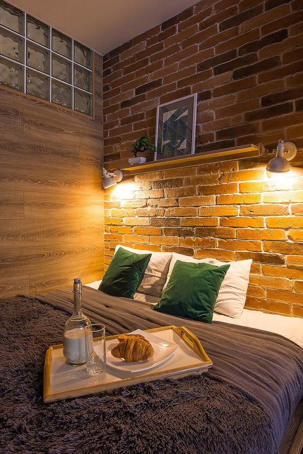 hình ảnh phòng ngủ nhỏ được trang trí với tường gạch đầu giường, đèn chiếu sáng, gối màu xanh lá