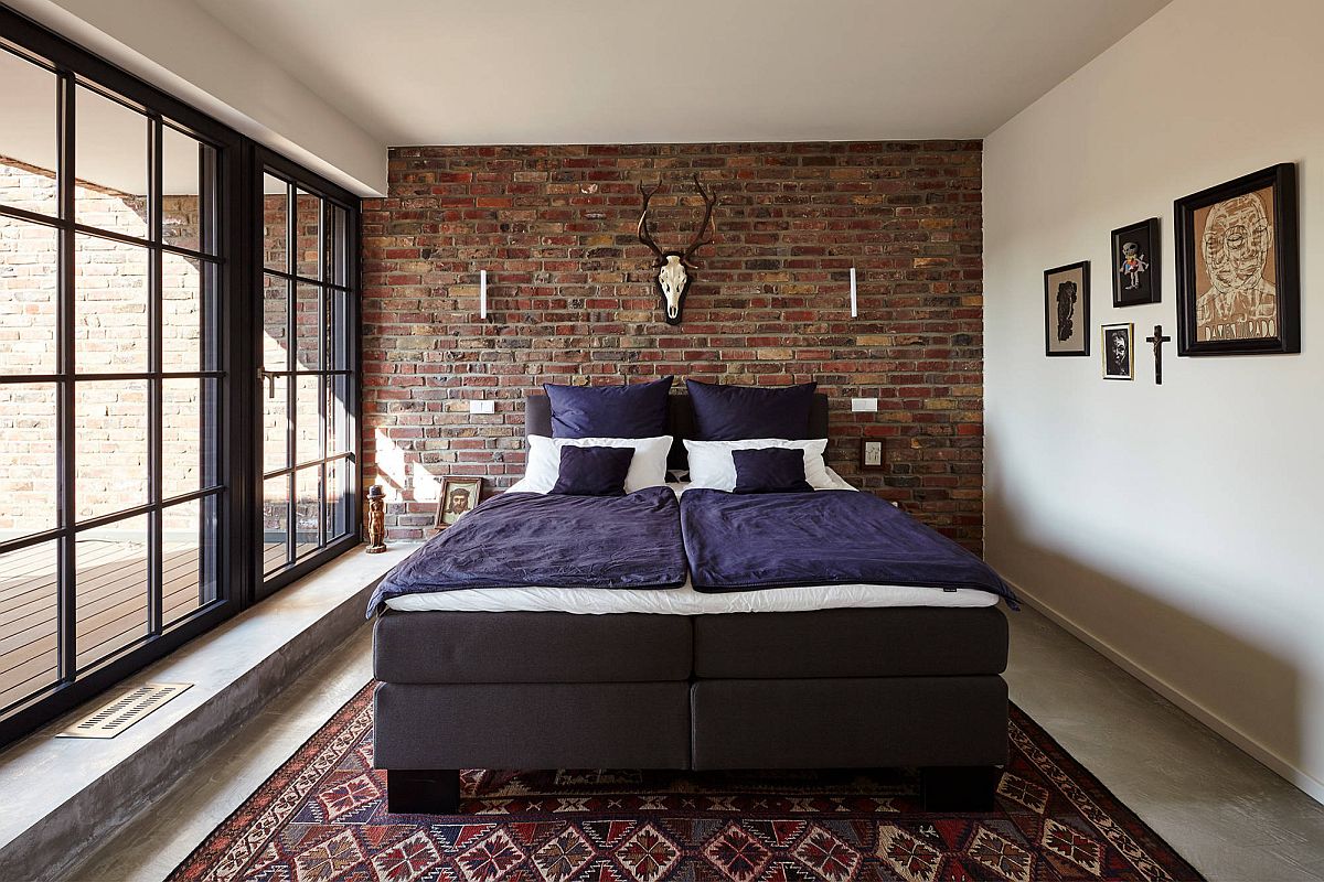 hình ảnh mẫu phòng ngủ phong cách công nghiệp hiện đại với tường gạch thô đầu giường, ga gối màu tím, thảm thổ cẩm