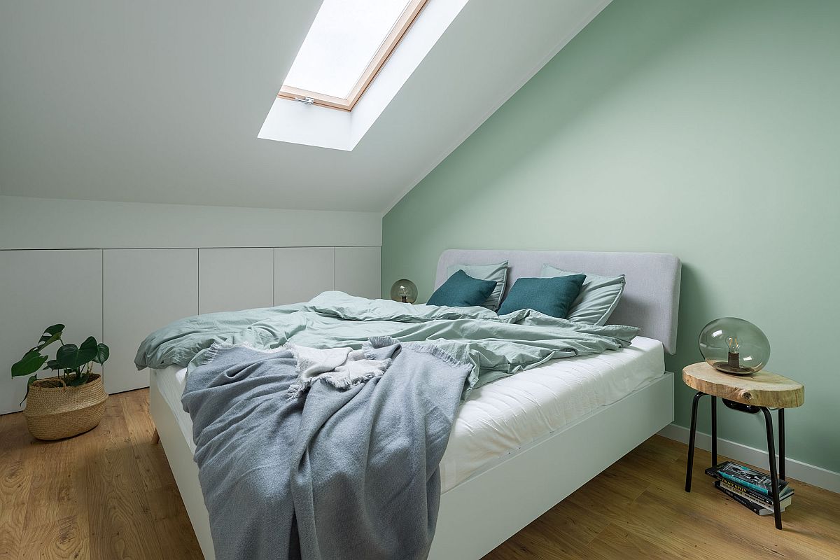 hình ảnh phòng ngủ tầng áp mái căn hộ 52m2 với tông màu xanh bạc hà chủ đạo, cửa sổ mái bằng kính, cây xanh trang trí