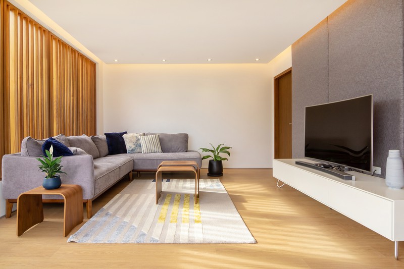 hình ảnh phòng khách nhà 3 tầng với sofa xám, bàn trà gỗ, kệ tivi màu trắng, cây xanh trang trí