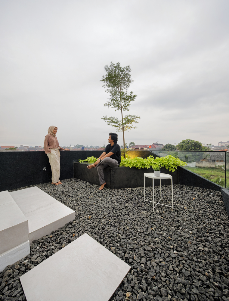 hình ảnh cặp đôi trẻ đang trò chuyện trên sân thượng, sàn rải đá dăm nhỏ, bàn trà tròn, bồn cây xanh