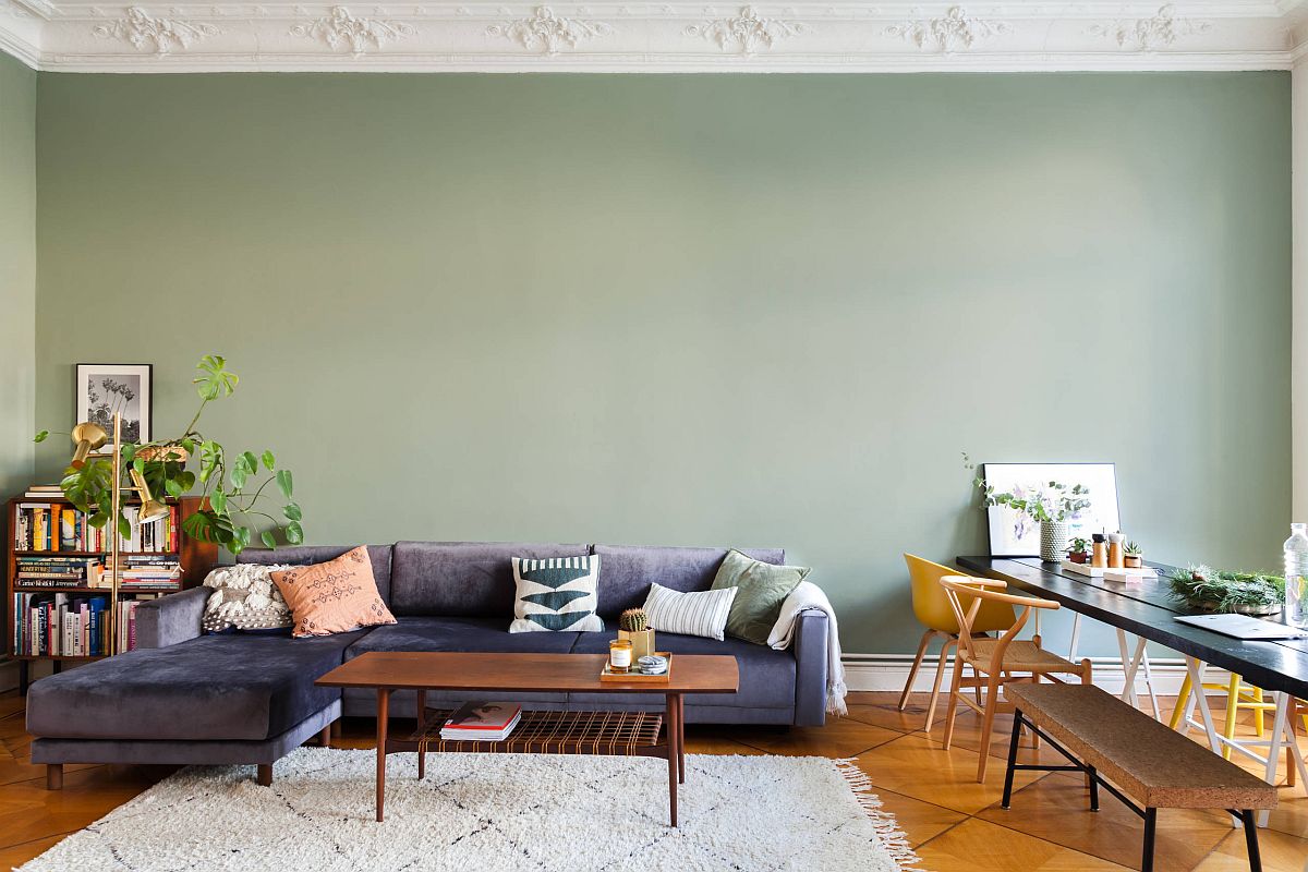 hình ảnh phòng khách với tường sơn màu xanh mint đậm, ghế sofa tím, bàn tà gỗ, thảm trải, cạnh đó là bàn ghế ăn