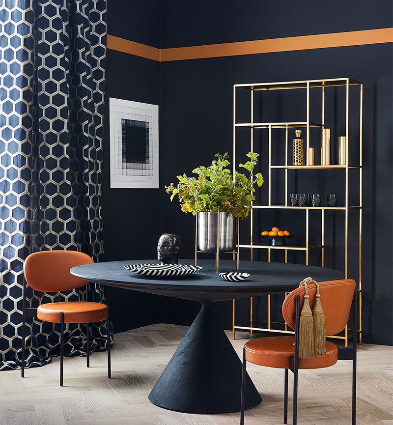hình ảnh một căn phòng với tường và bàn màu xanh than, rèm cửa họa tiết hình học, ghế ngồi bọc da màu vàng da bò