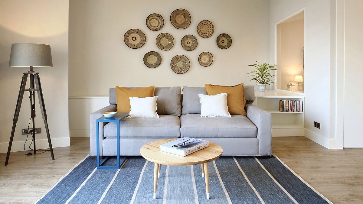 Hình ảnh phòng khách căn hộ nhỏ màu trắng xanh với sofa xám, thảm trải kẻ sọc xanh, trang trí tường ấn tượng