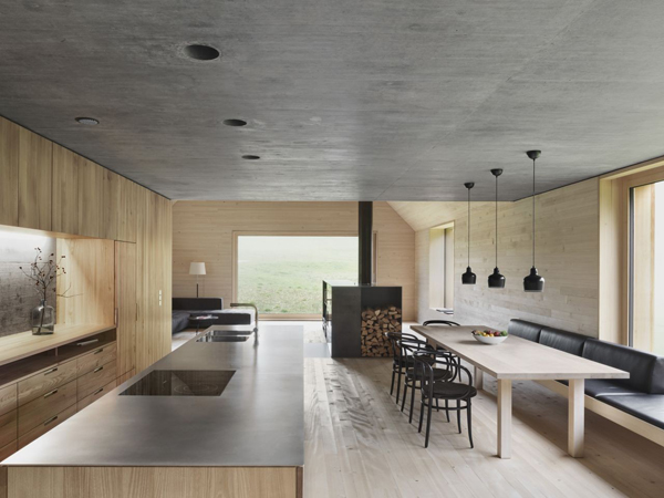 Hình ảnh phòng bếp ăn kết hợp với trần xi măng xám, tủ gỗ mộc mạc, đèn thả trần màu đen tạo điểm nhấn cho khu vực bàn ăn