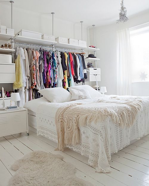 hình ảnh một phòng ngủ nhỏ màu trắng với đầu giường là giá kệ lưu trữ quần áo màu sắc