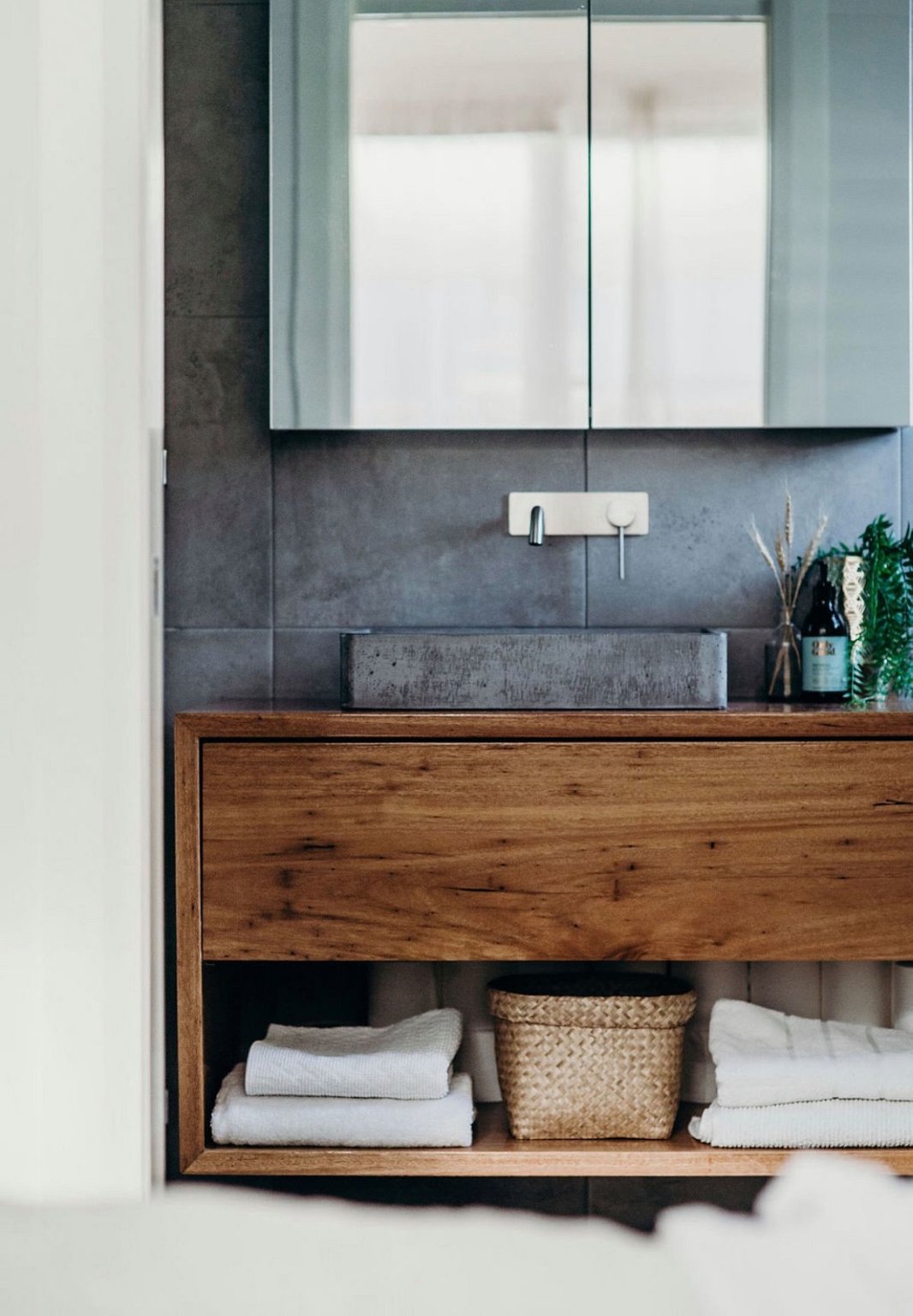 hình ảnh một góc phòng tắm mùa hè với tường bê tông xám sau gương soi, tủ gỗ mộc mạc