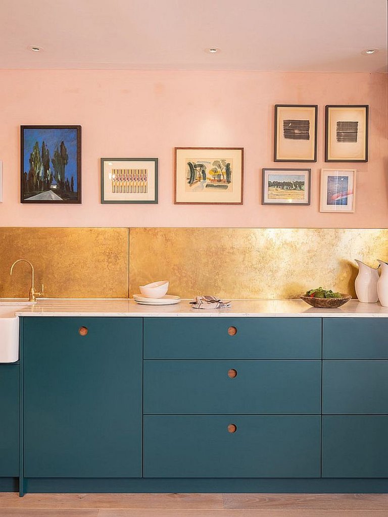 hình ảnh cận cảnh góc bếp đẹp với tường sơn màu hồng, mảng nhỏ ốp gạch vàng đồng, tủ bếp màu xanh dương, tranh treo tường tạo điểm nhấn