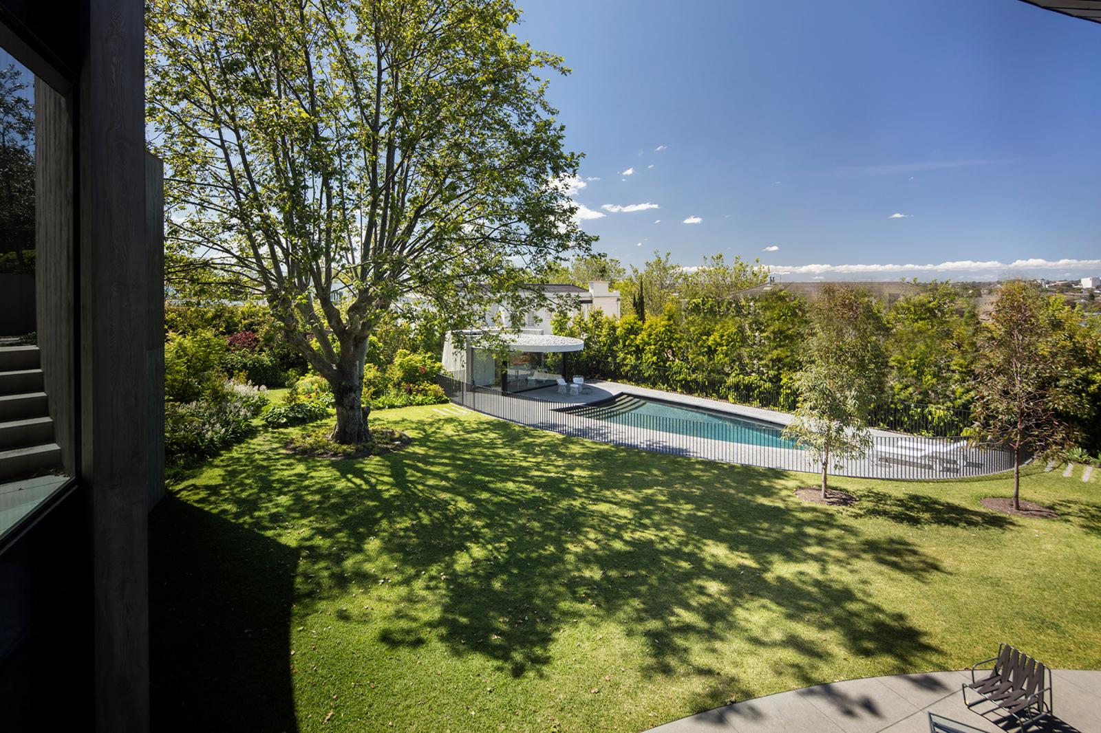 hình ảnh bể bơi bầu dục ở sân sau ngôi nhà có mái hình đĩa, thảm cỏ xanh mướt, cây cổ thụ tỏa bóng mát