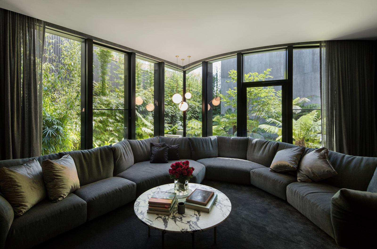 hình ảnh phòng sinh hoạt chung gia đình rộng rãi, tiện nghi với sofa ghi xám lớn, tường kính trong suốt nhìn ra vườn cây xanh tốt bên ngoài