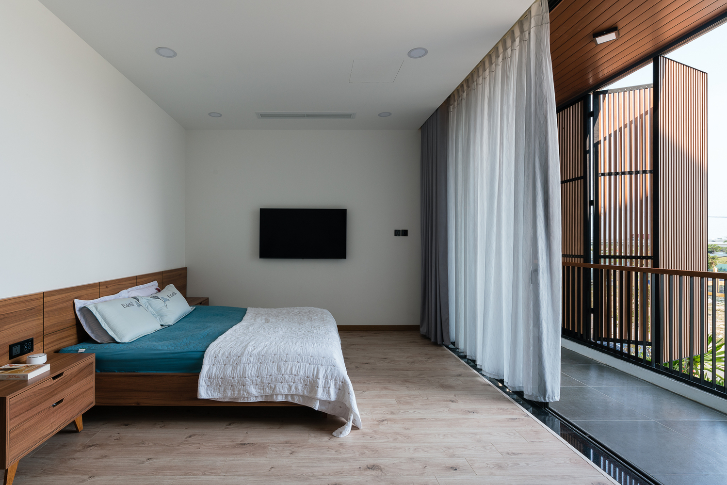 hình ảnh phòng ngủ phong cách tối giản với giường gỗ, ga màu xanh dương, hiên rộng thoáng, rèm cửa 2 lớp màu trắng