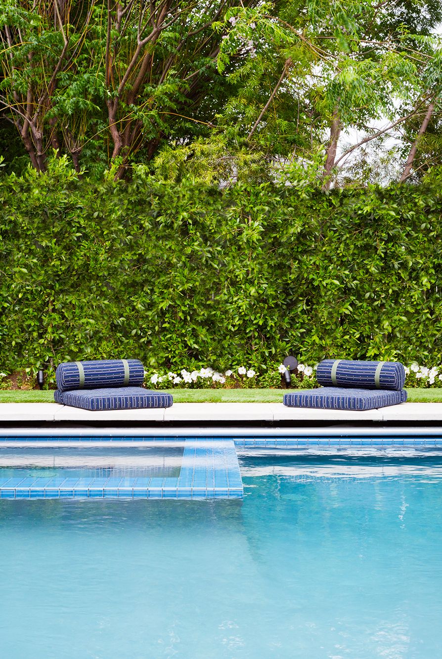 hình ảnh cận cảnh sàn hồ bơi nổi bật với hai đệm ngồi màu xanh coban, phía sau là tường cây xanh