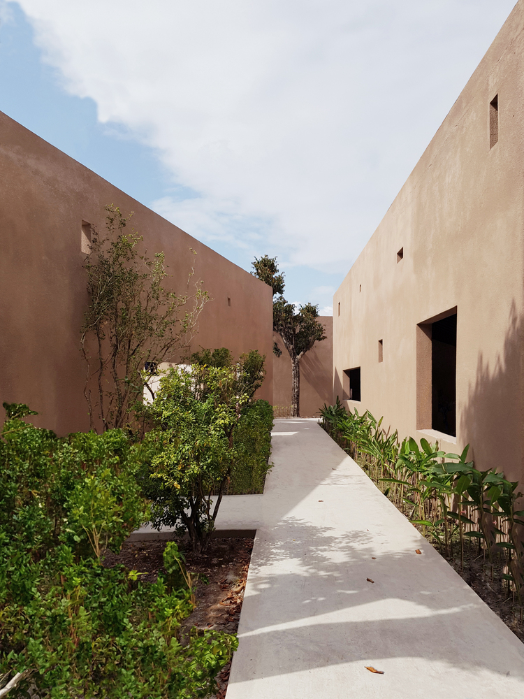 hình ảnh lối đi sân vườn lát bê tông, hai bên trồng cây xanh, cạnh đó là hệ tường xuyên suốt công trình