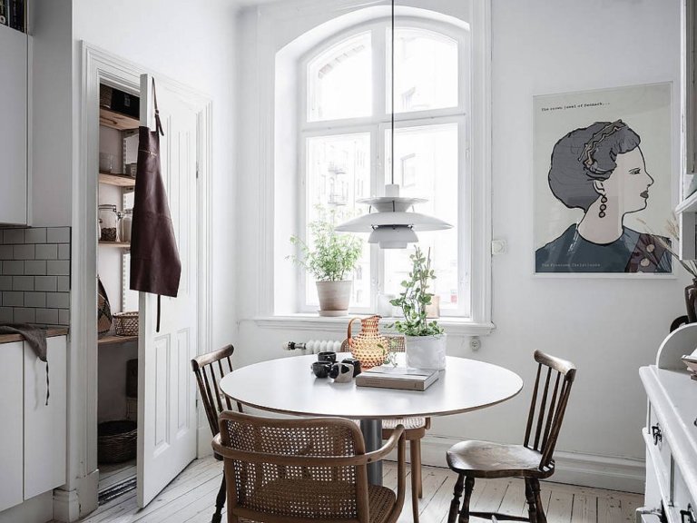 hình ảnh phòng ăn nhỏ màu trắng với tranh tường ấn tượng, bàn tròn, ghế mây, cửa sổ kính lớn, vài chậu cảnh trang trí