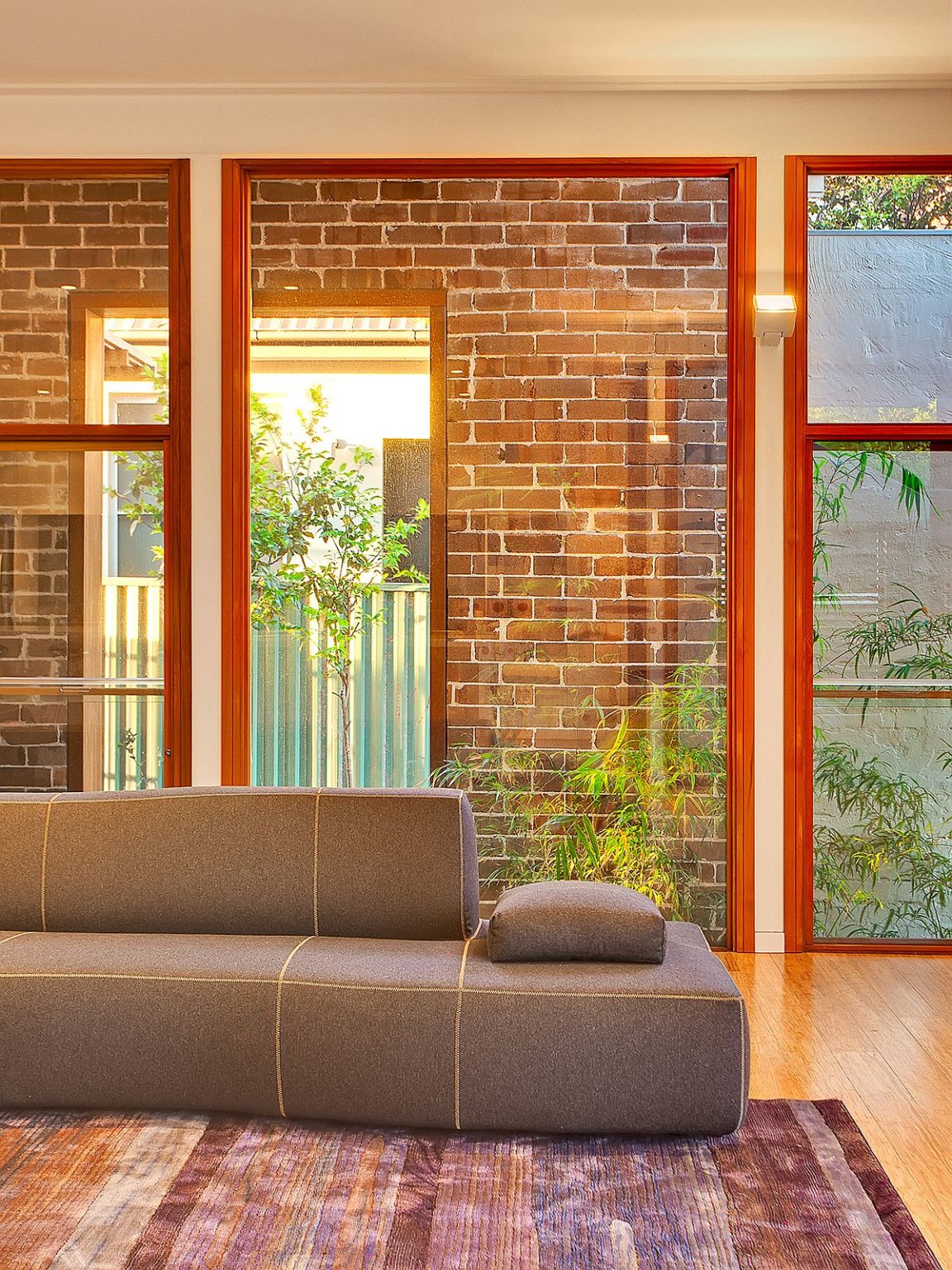 hình ảnh một góc phòng sinh hoạt chung với sofa ghi xám, tường gạch, cửa kính trong suốt