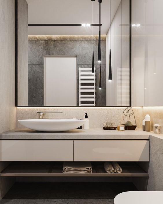 hình ảnh một góc phòng tắm có thiết kế đơn giản, nổi bật với khung gương lớn treo trên bồn rửa mặt, phản chiếu bộ đèn thả trần hiện đại