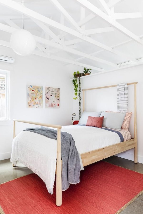 hình ảnh toàn cảnh phòng ngủ nhỏ màu trắng với dầm sơn trắng, gối tựa và thảm trải màu hồng đất, cây xanh trang trí