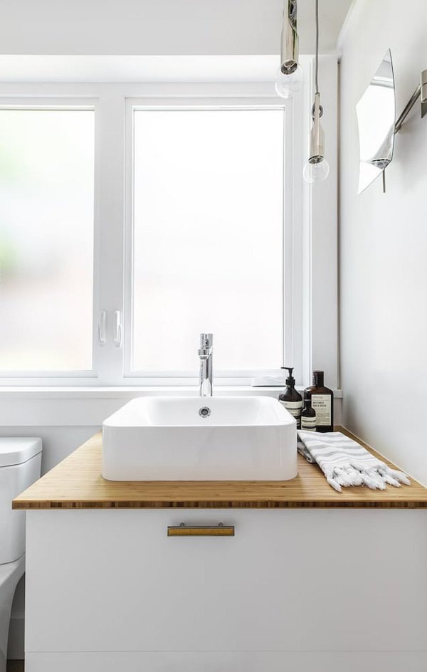 hình ảnh một góc phòng tắm với bề mặt bàn chậu rửa bằng gỗ, cửa sổ kính ngập tràn ánh sáng