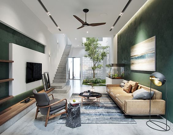 hình ảnh phòng khách nhà ống 2 tầng với tường sơn màu xanh lá, sofa màu be, tivi gắn tường, thảm trải họa tiết xanh dương