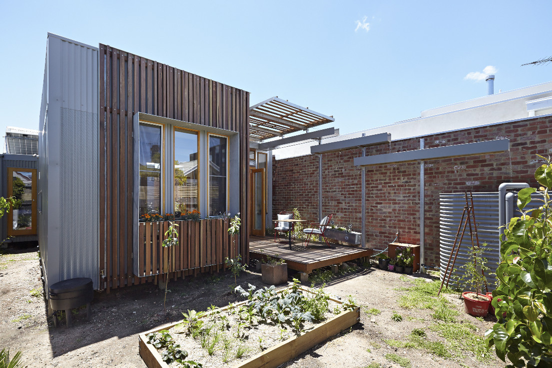 hình ảnh một ngôi nhà nhỏ với mặt tiền ốp lam gỗ, cửa sổ kính, tường gạch, sân vườn trồng rau