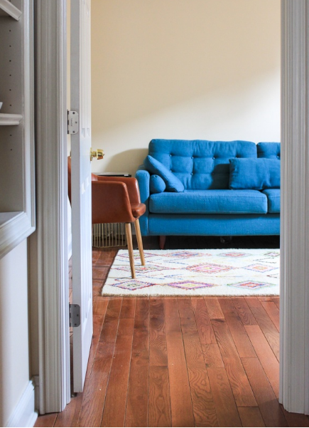 hình ảnh phòng khách với bức tường trống đơn điệu, sofa màu xanh da trời, ghế bành màu da bò ngay cạnh