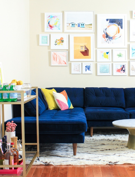 hình ảnh một góc phòng khách với sofa nhung xanh dương mềm mại, tranh treo tường, kệ gỗ lưu trữ ngay cạnh