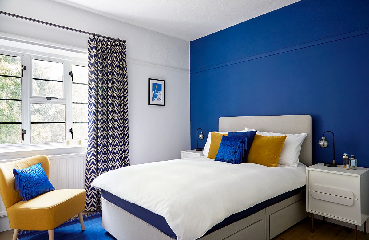 hình ảnh phòng ngủ với tường đầu giường sơn xanh, ghế ngồi màu vàng, rèm cửa xanh trắng
