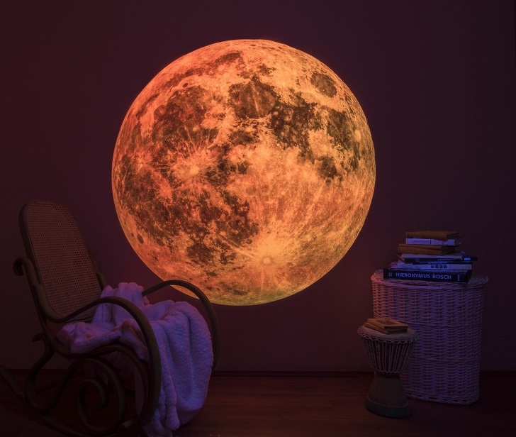 hình ảnh hình in mặt trăng phát sáng trên tường màu tím, cạnh đó là ghế ngồi thư giãn, bàn mây tre đan đặt chồng sách