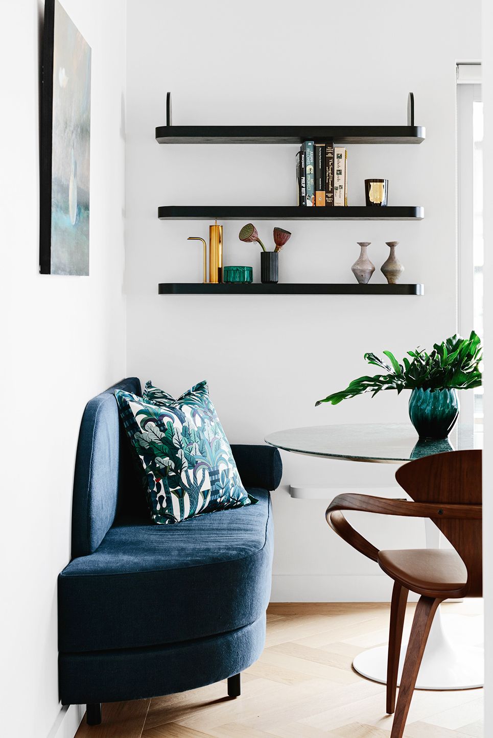 hình ảnh phòng ăn nhỏ đẹp với bàn tròn, ghế sofa bọc vải màu xanh dương, kệ gỗ màu đen nổi bật trên nền tường trắng