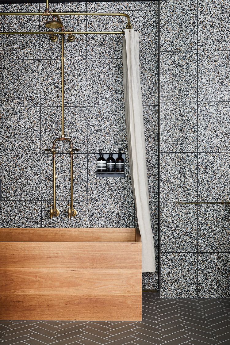 hình ảnh góc phòng tắm với gạch ốp tường giả đá, gạch lát sàn xương cá, vòi sen, ống nước bằng đồng