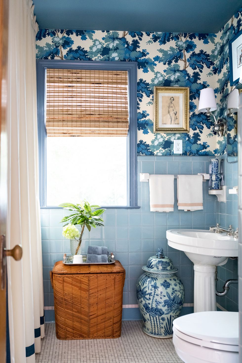 hình ảnh phòng tắm phong cách Retro với gạch ốp tường màu xanh da trời, giấy dán tường họa tiết lá cây cối màu xanh, bình gốm trang trí