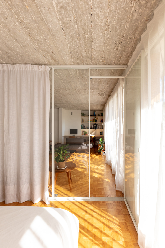 hình ảnh một góc phòng ngủ với ga gối màu trắng, cửa kính nhìn ra phòng khách bên ngoài của căn hộ 42m2