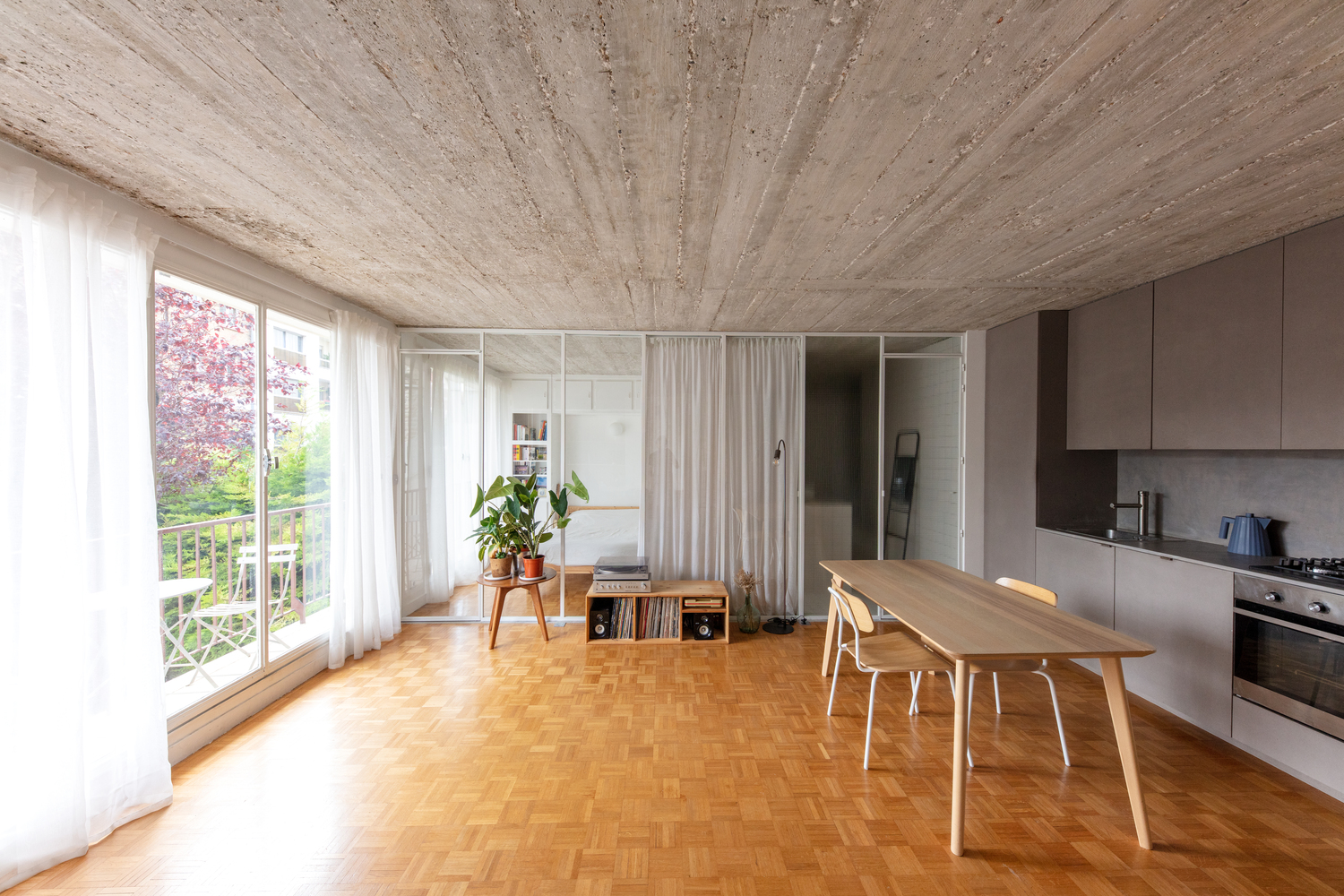 hình ảnh khu vực bếp nấu và phòng ăn trong căn hộ 42m2 với hệ tủ màu ghi xám, trần ốp gỗ cùng tông, sàn gỗ, cửa kính lớn