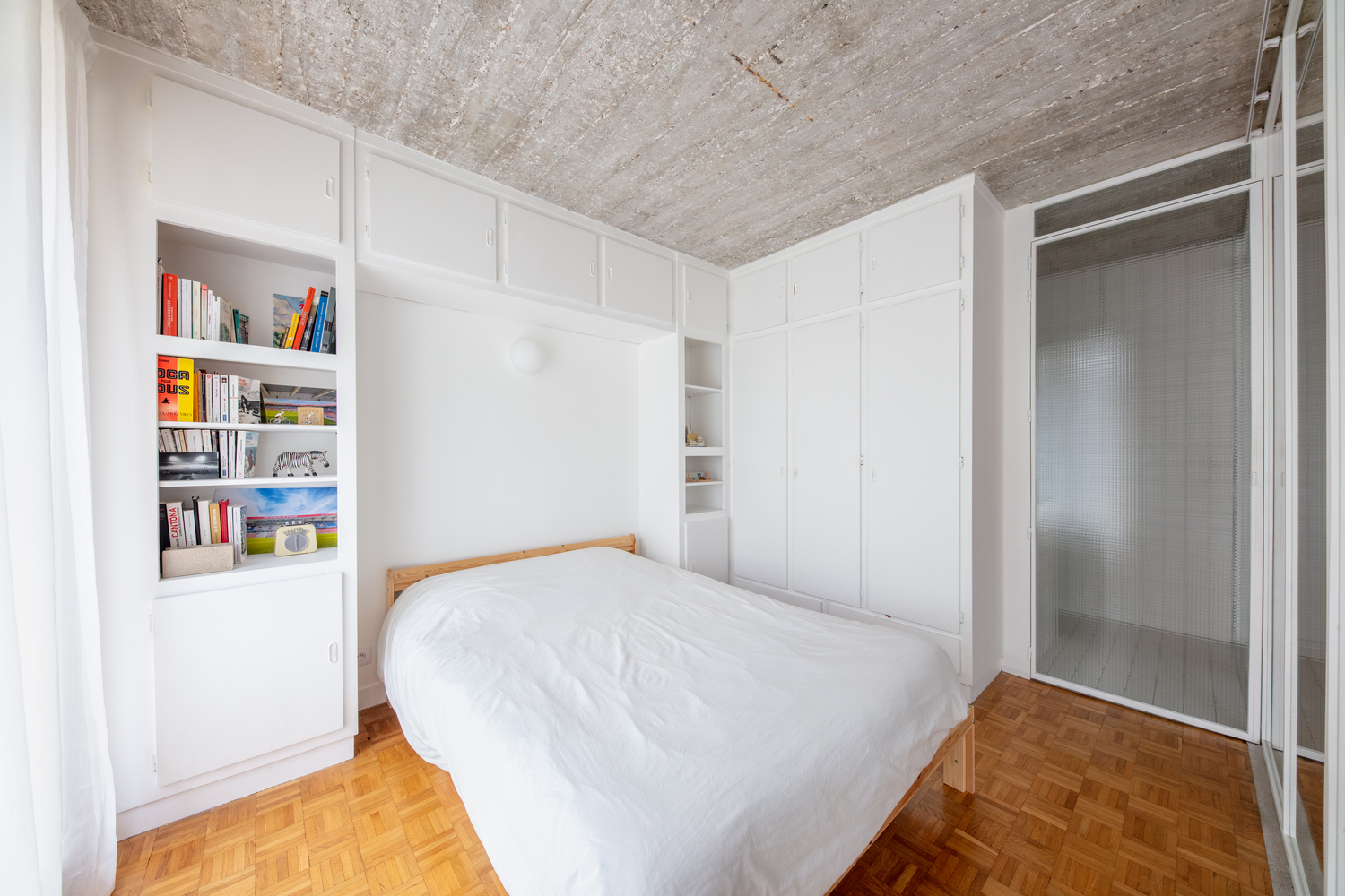 hình ảnh toàn cảnh phòng ngủ với ga gối màu trắng, tủ kệ lưu trữ cùng tông, sàn gỗ màu sáng
