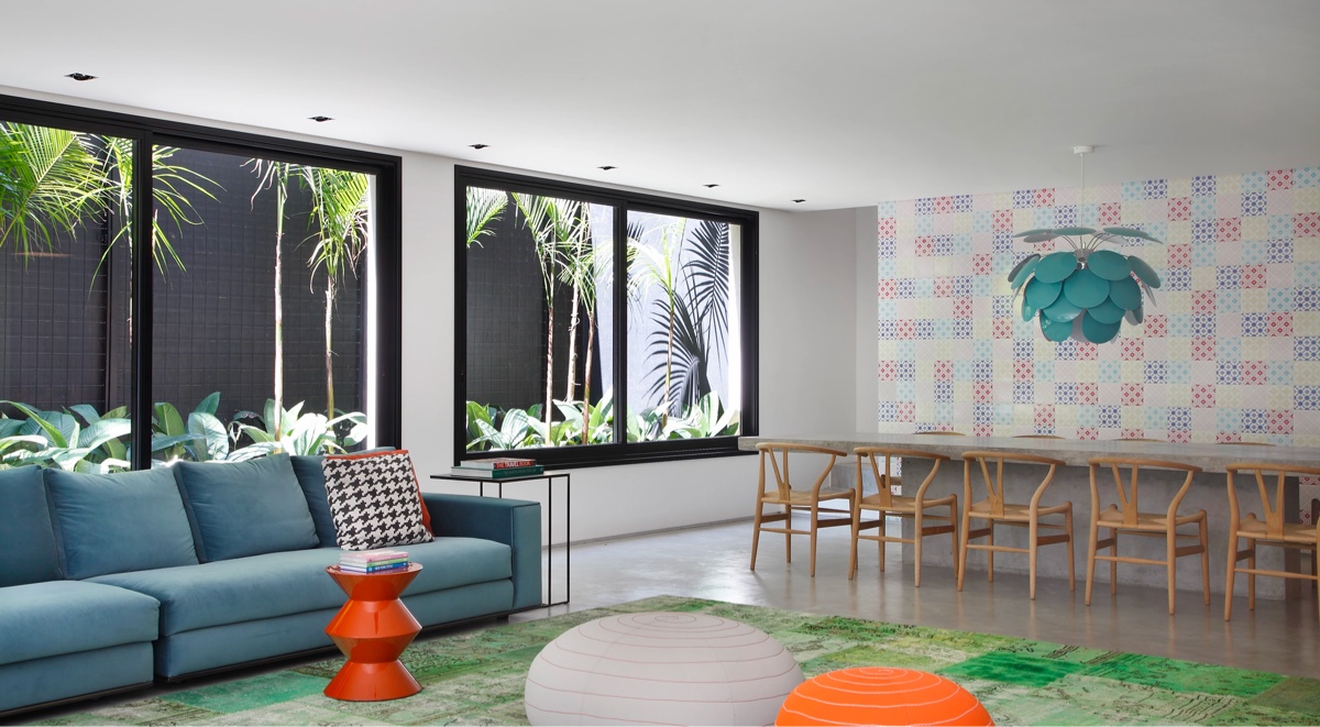 hình ảnh phòng khách được thiết kế liên thông phòng ăn với ghế sofa màu xanh dương, bàn ghế băng bằng gỗ mộc mạc, cửa sổ kính lớn, bên ngoài là sân vườn xanh mát