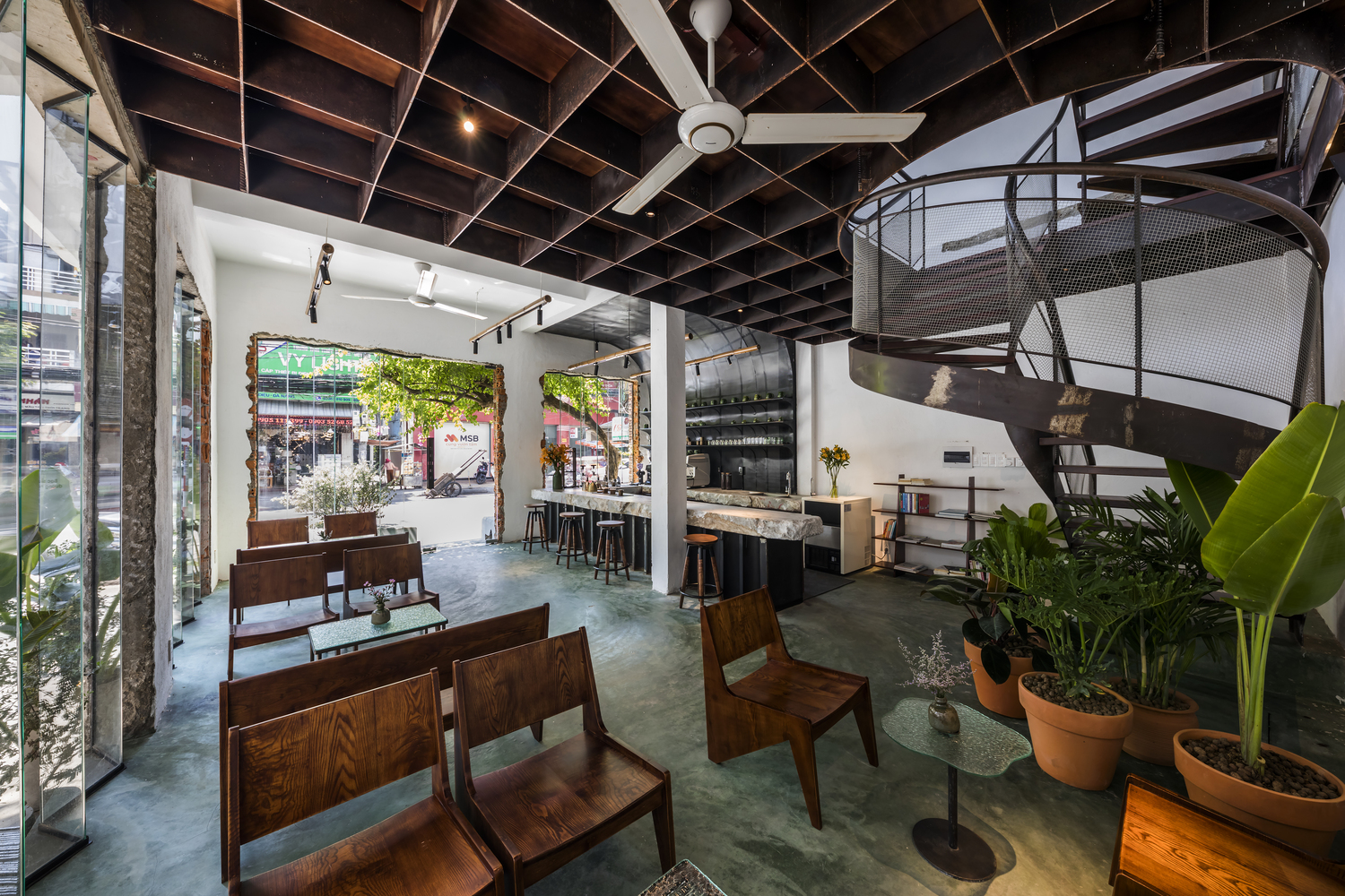 hình ảnh tầng trệt quán cà phê với sàn bê tông màu xanh ngọc, dầm gỗ sẫm màu, bàn ghế gỗ nhỏ gọn phong cách truyefn thống, cầu thang uốn lượn, cửa kính trong suốt