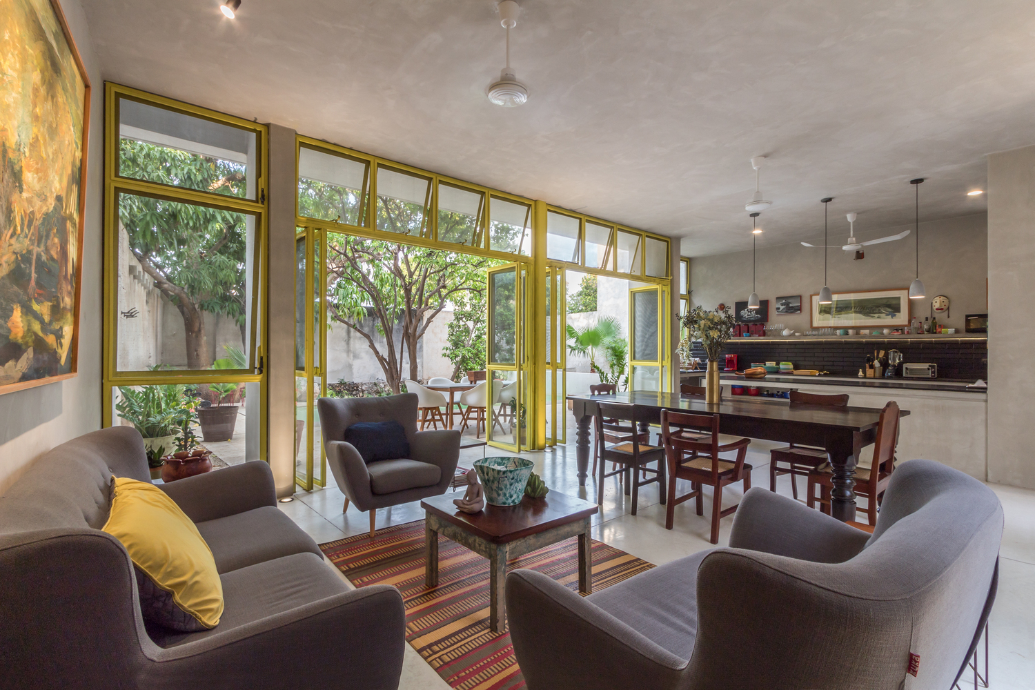 hình ảnh phòng khách liên thông phòng ăn và bếp trong nhà bê tông với cửa kính lớn, khung vàng nổi bật