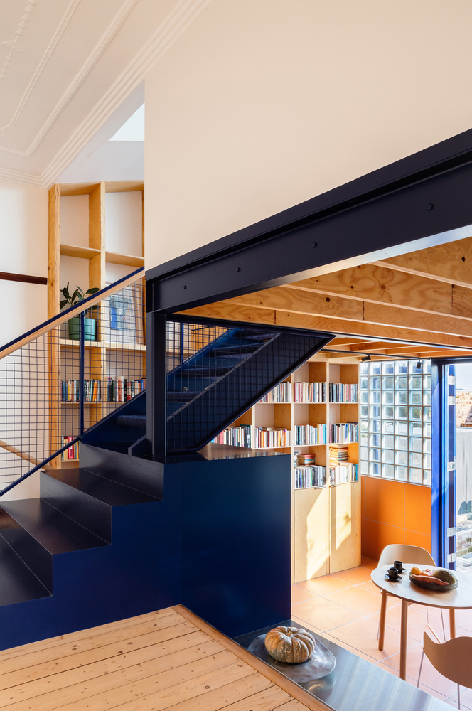 hình ảnh khu vực tầng trệt với nội thất gỗ thông, cầu thang màu xanh dẫn lên phòng đọc