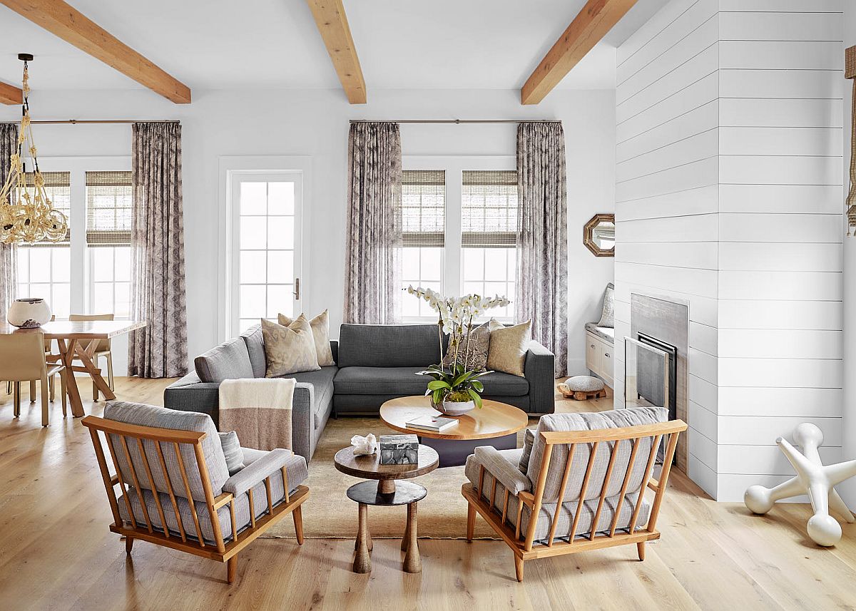 hình ảnh phòng khách ngôi nhà phong cách bãi biển với bàn ghế khung gỗ bọc nệm màu ghi xám, dầm gỗ lộ thiên, cửa kính, rèm cửa buông rũ xuống sàn nhà