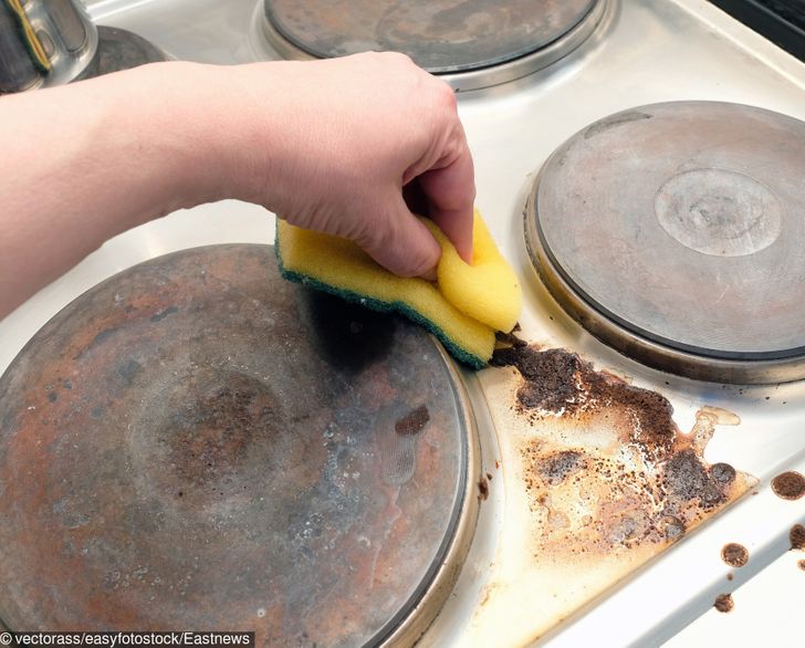 hình ảnh một người đang tẩy rửa các vết bẩn bám trên bề mặt bếp nấu