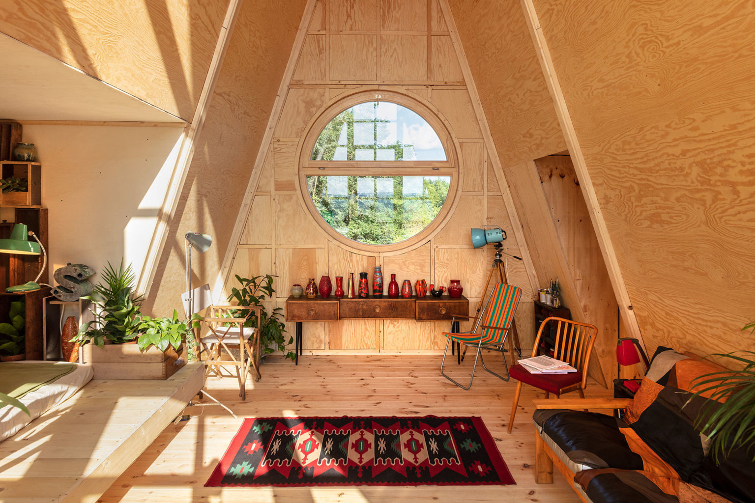 hình ảnh không gian sinh hoạt bên trong nhà cabin với bàn ghế gỗ nhỏ gọn, cửa sổ tròn, thảm trải màu sắc