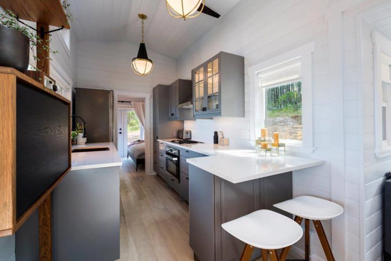hình ảnh phòng bếp nhà di động với tủ bếp màu xám, mặt bàn bằng đá thạch anh trắng, quầy bar ăn sáng cho hai người, đèn thả ấm áp