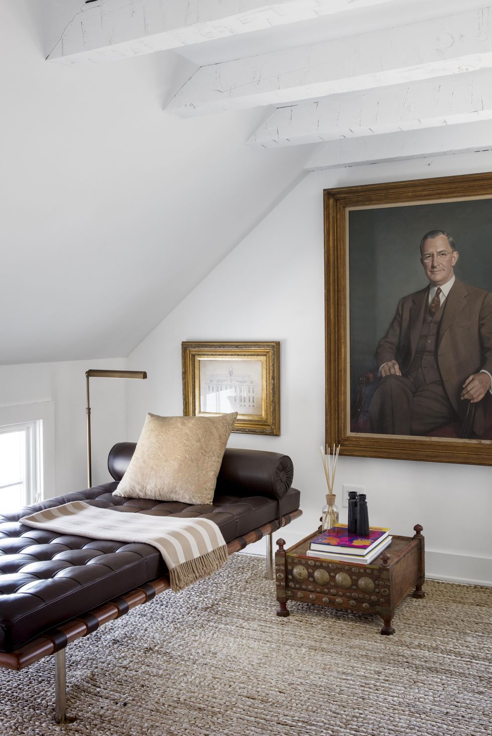 hình ảnh phòng khách tầng áp mái với tường và trần sơn trắng, sofa giường bọc da màu đen, cạnh đó là bàn phụ, tranh chân dung cỡ lớn treo tường