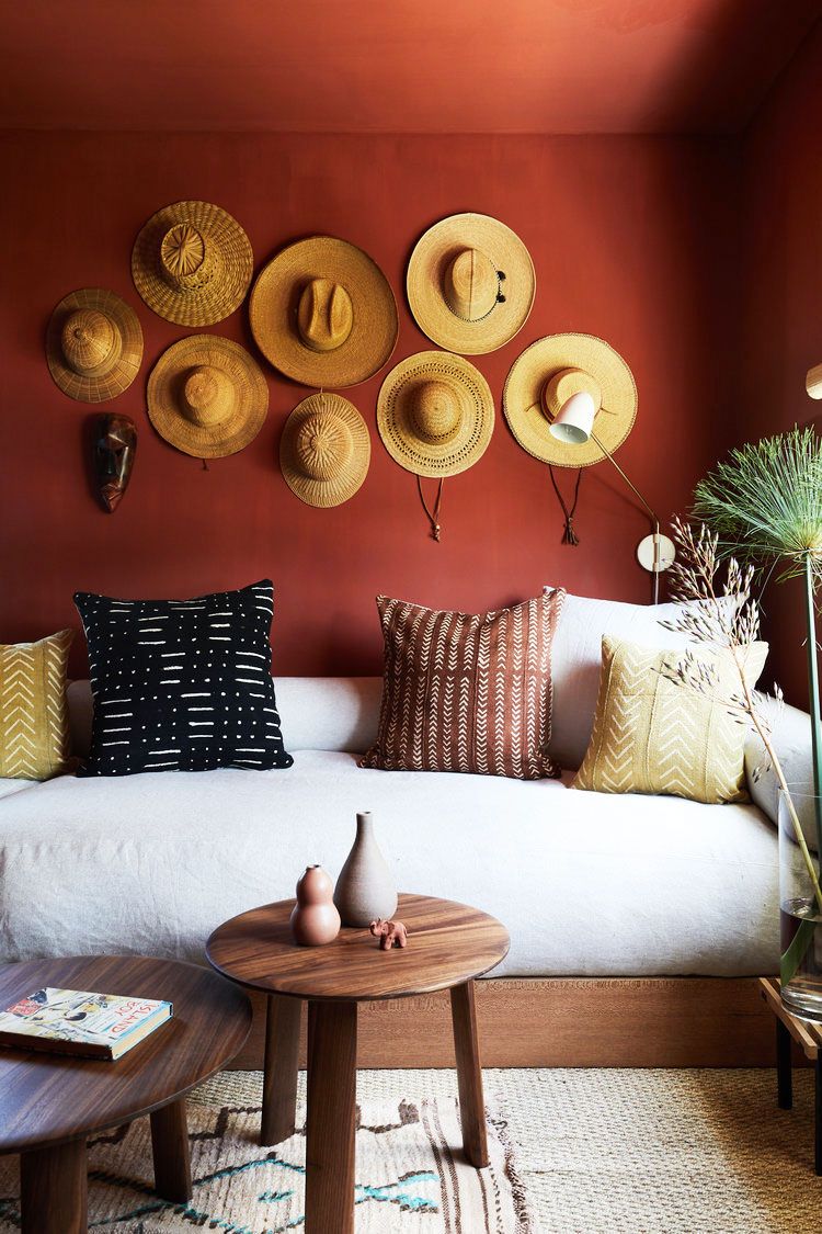 hình ảnh phòng khách nhỏ với tường sơn màu đỏ cam, trang trí bộ sưu tập mũ cói, sofa màu trắng, bàn trà đôi bằng gỗ